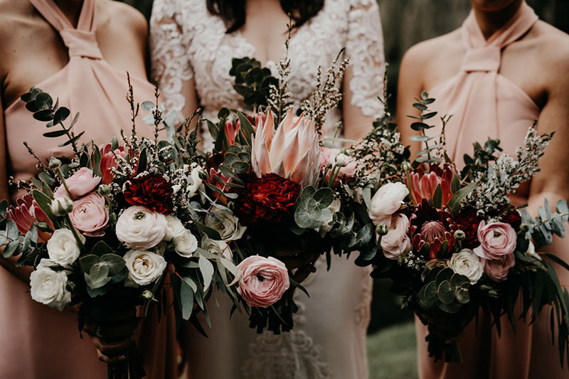 Bride and bridesmaids holding deep, rich wedding flower bouquets.