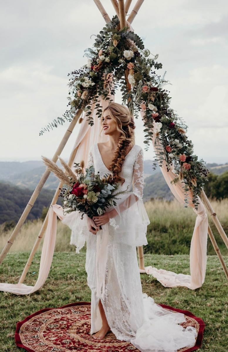 Boho bride holding a gorgeous bouquet in front of an arch with hanging flowers.