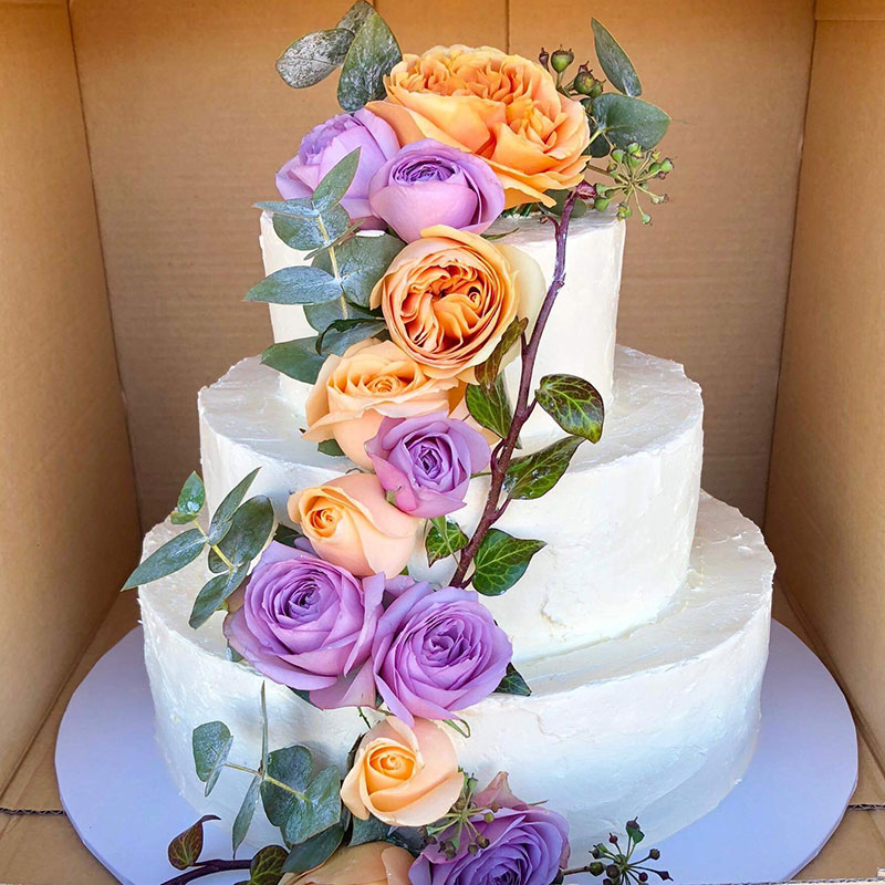 White wedding cake with colourful roses draping it.