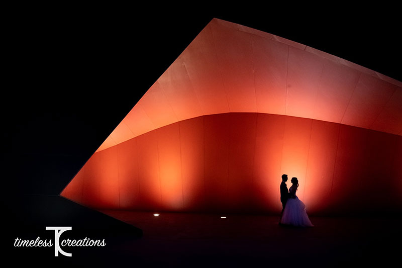 Bride and Groom stand in front of a lit up red coloured structure.
