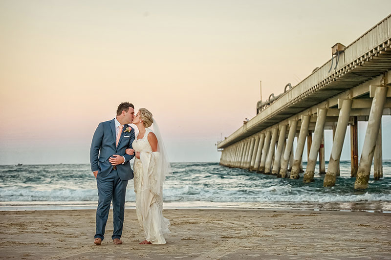 Bride and groom kissing next to pier at Surfers Paradise beach.