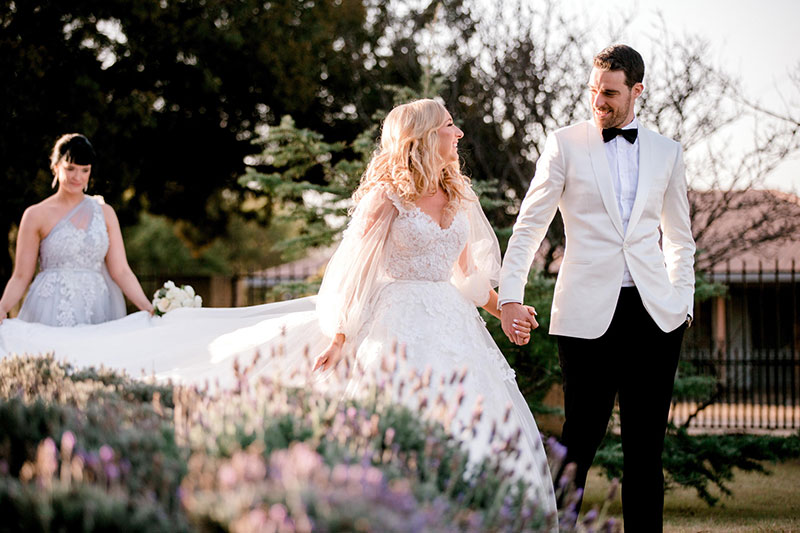 Groom in stylish White jacket and Black bowtie and pants walking with his beautiful Bride in White. 