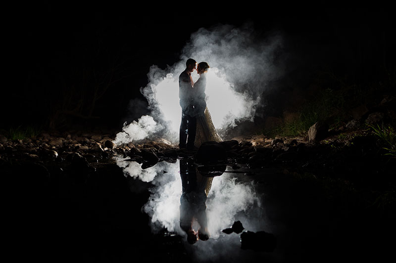 Photo of couple at night standing in front of a light and smoke bomb.