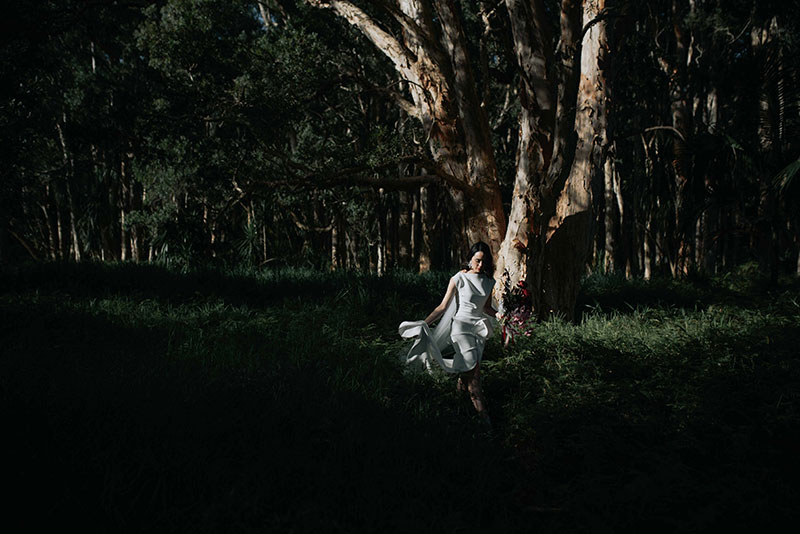 Moody photo showing a bride holding flowers walking near trees in the dark.