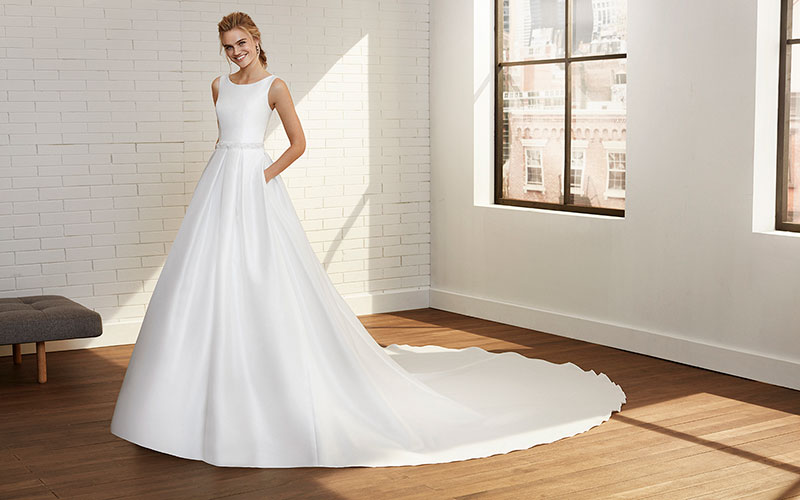 Model posing in room, wearing a crisp white bridal gown from Rosa Clara.