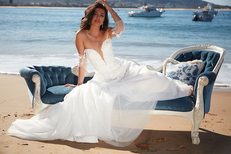 Angelina bridal gown by Sarah Joseph Couture on model sitting on a lounge on the beach.