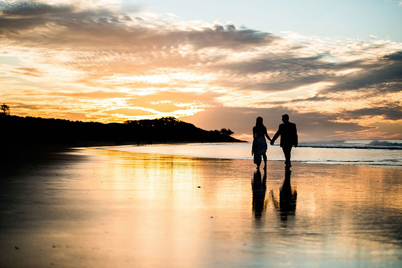 Couple walking along Stradbroke Island beach at sunset.