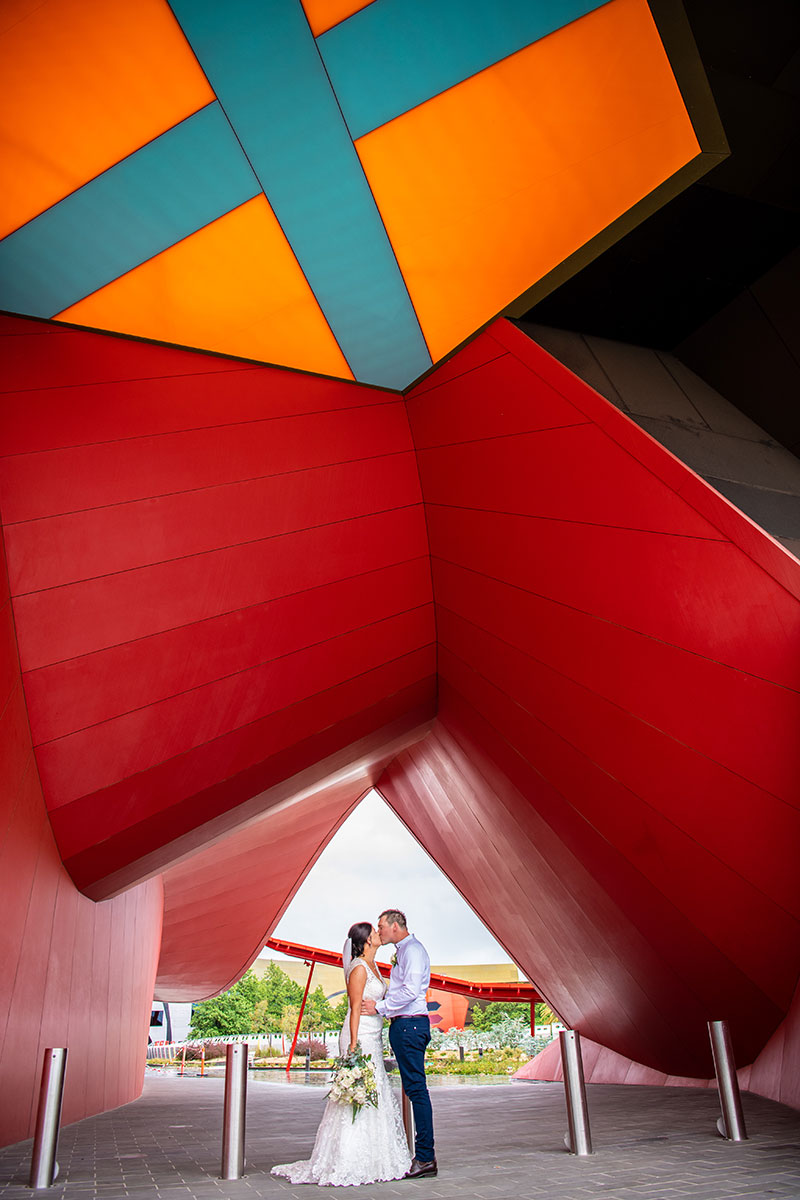 Bride and Groom kiss under a colourful structure.