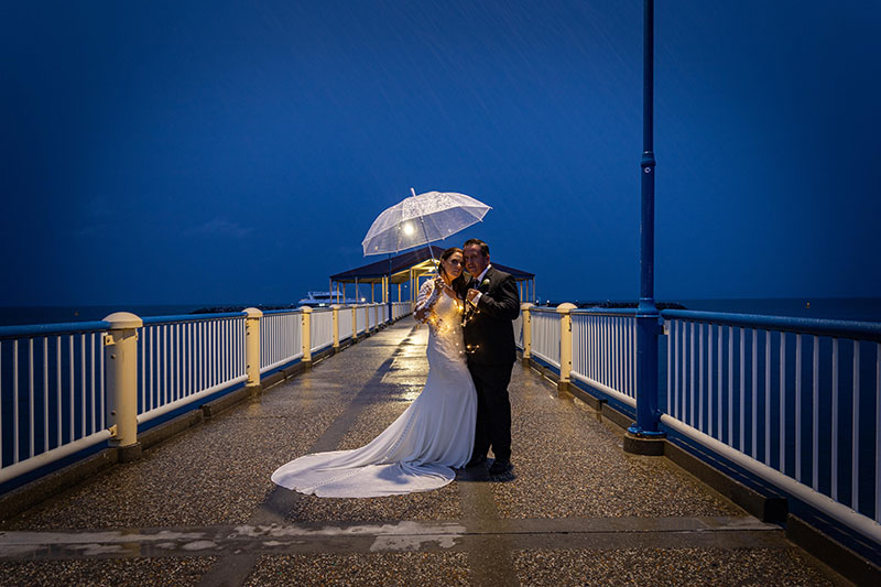 Bride and Groom posing on pier, holding an umbrella.