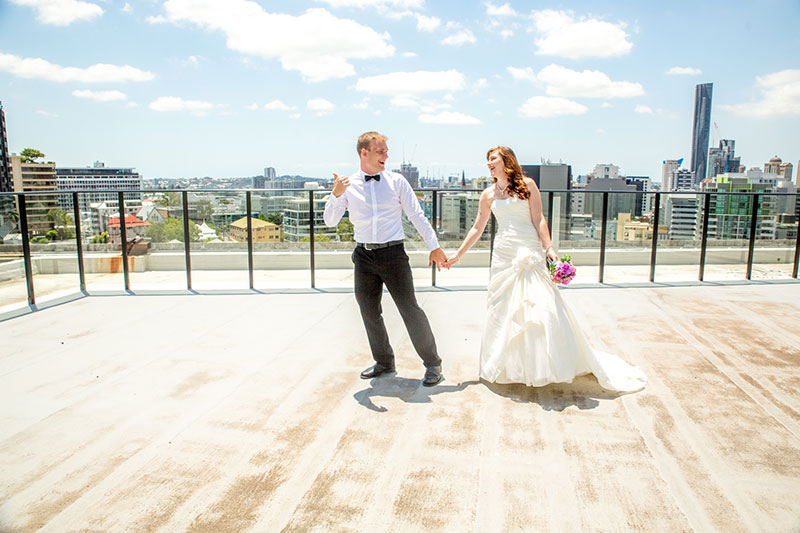 Bride and Groom on balcony dancing on a bright day, with high rise buildings in the background.