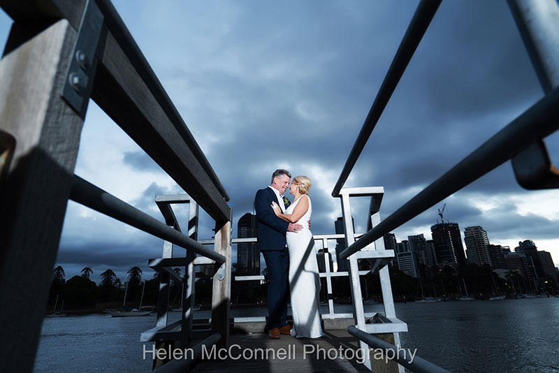 Bride and Groom on pier with the city and storm clouds in the background..