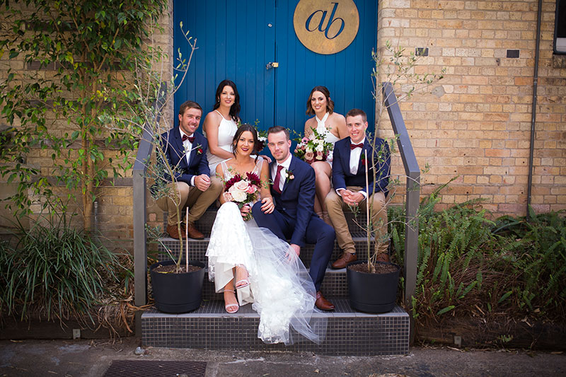 Bridal party sitting on stairs with a bright blue door behind.