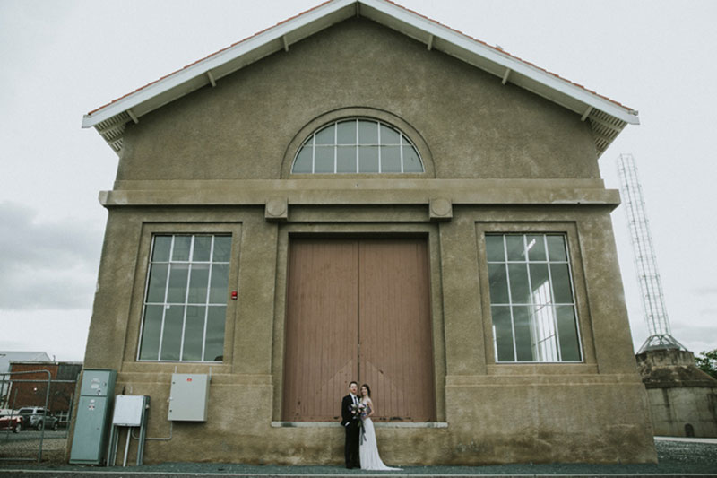 Bride and Groom stand in front of a large, old building.
