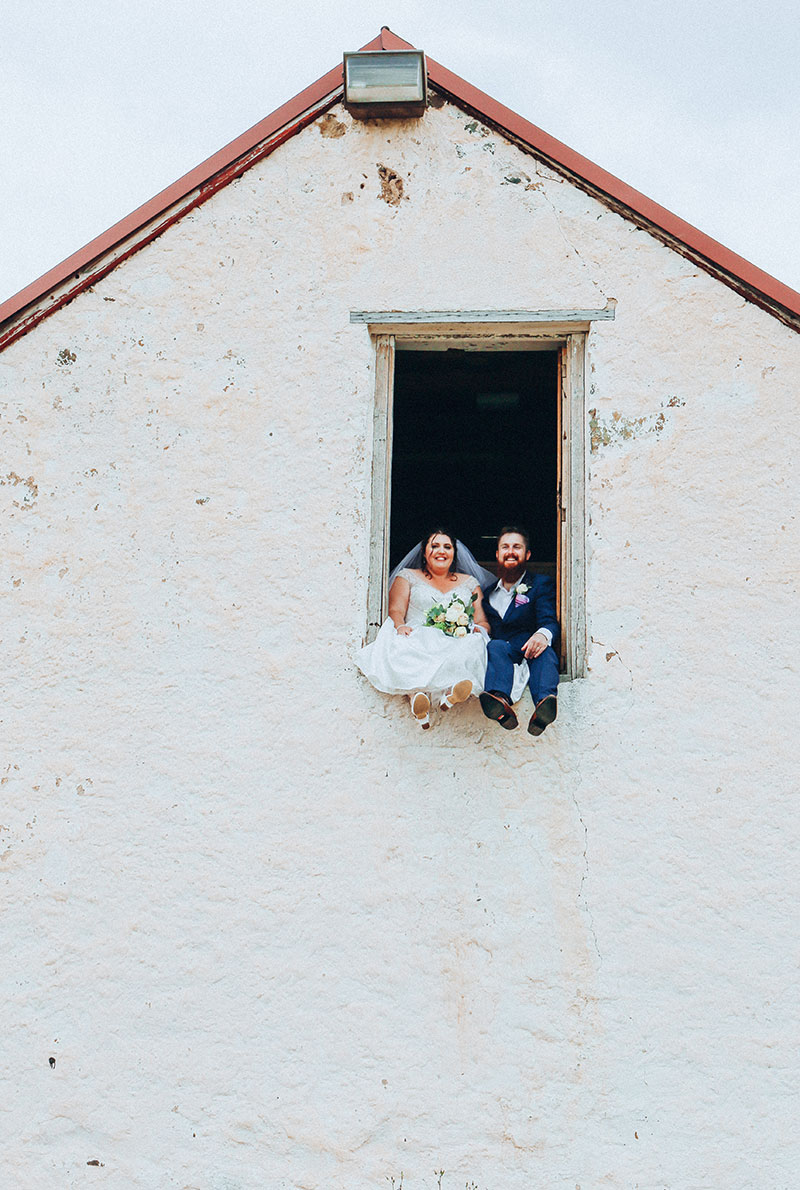 Happy Bride and Groom sit perched high in a window.