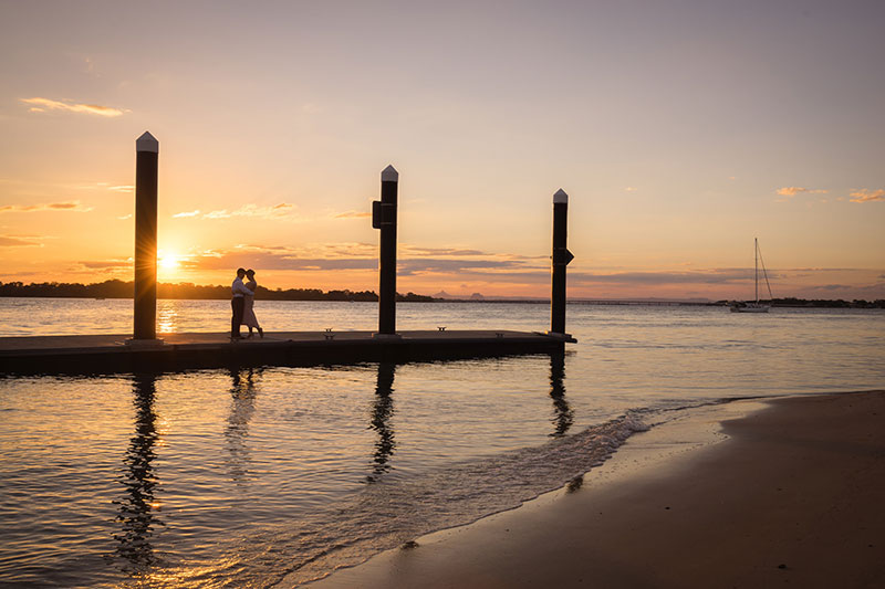 Couple on jetty under the setting sun.