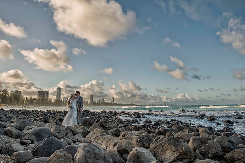 Couple standing amongst lots of rocks at the beach.