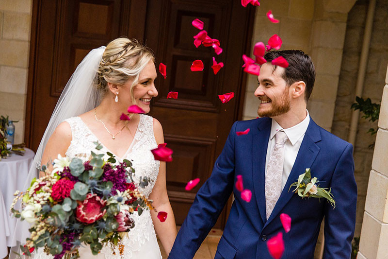 Rose petals thrown as Groom in Navy Suit and Bride in white are married.