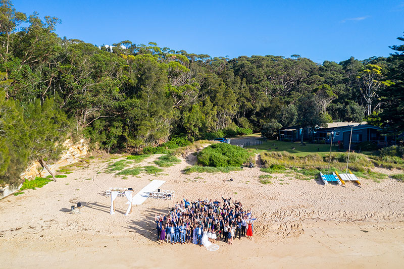 Drone taking photos of wedding party below in beach setting.