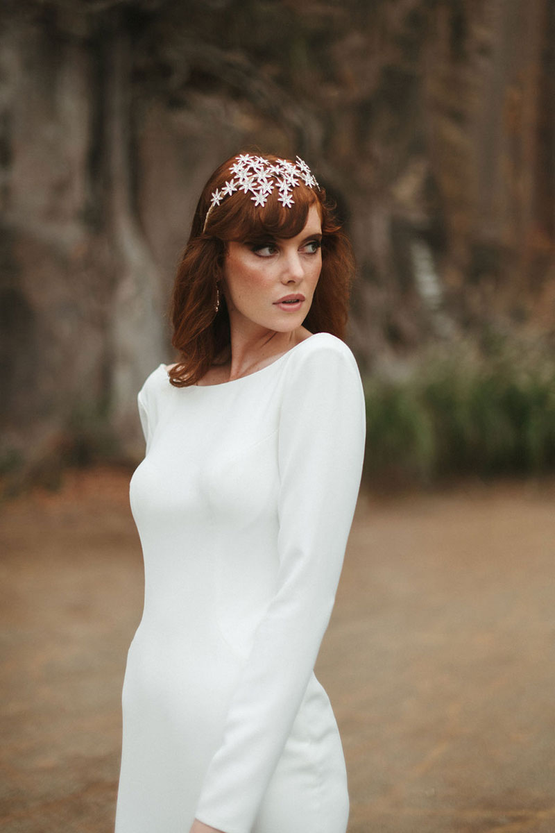 Close up of a bride with hairpiece wearing a long sleeved gown.