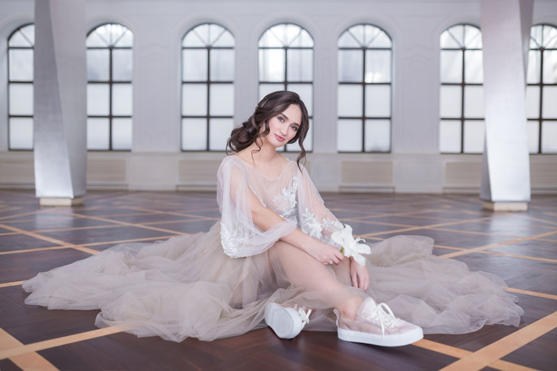 Girl sitting on floor wearing wedding sneakers.