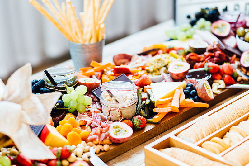 Grazing board with an assortment of fruit, vegies, cold meats, dips, breadsticks and biscuits.