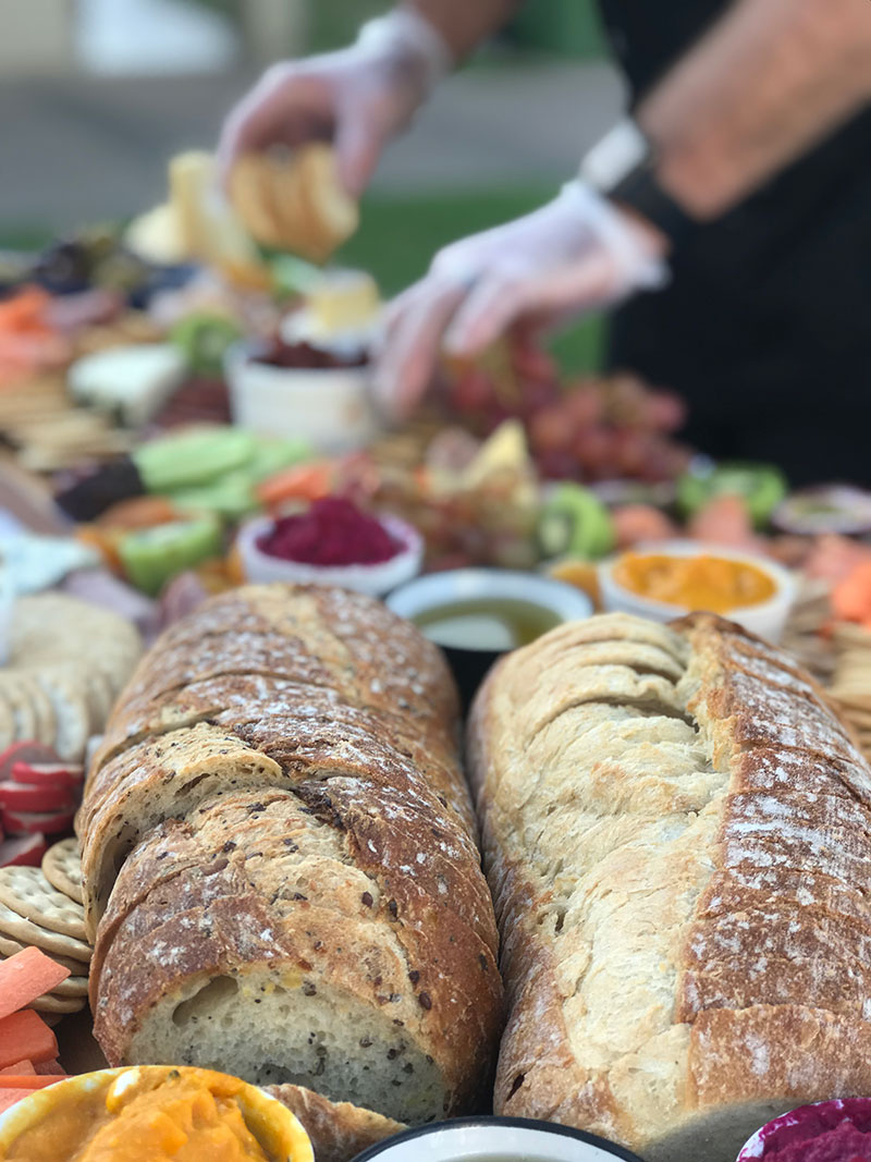 Grazing platter board showing crusty bread and food being set up and maintained.