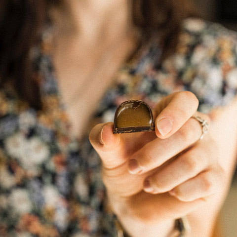 Woman holding a chocolate which shows the filling inside the chocolate.