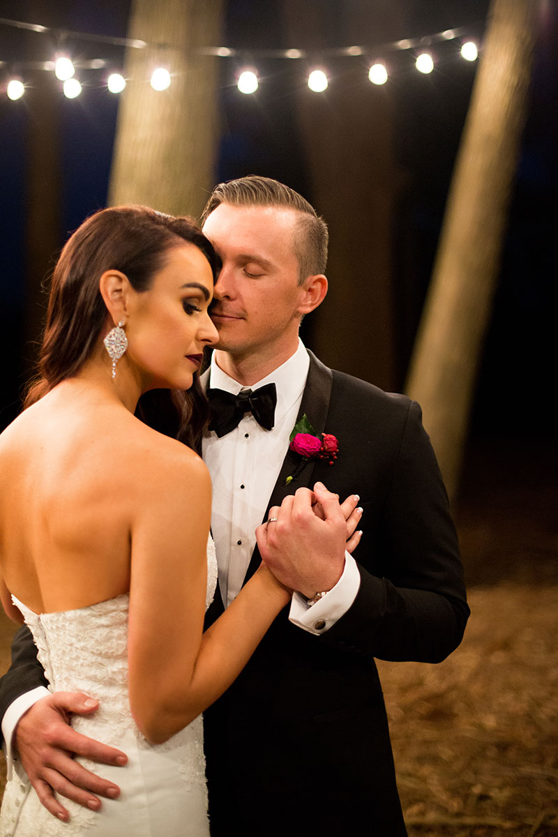 Bride and Groom dancing together under a string of lights at night.