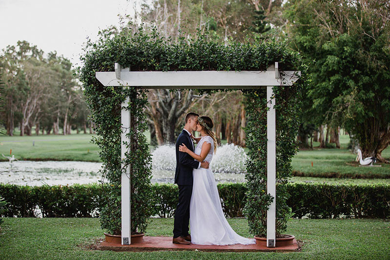 Bride and Groom kissing under an arbour on manicured lawns at Redland Bay Golf Club.