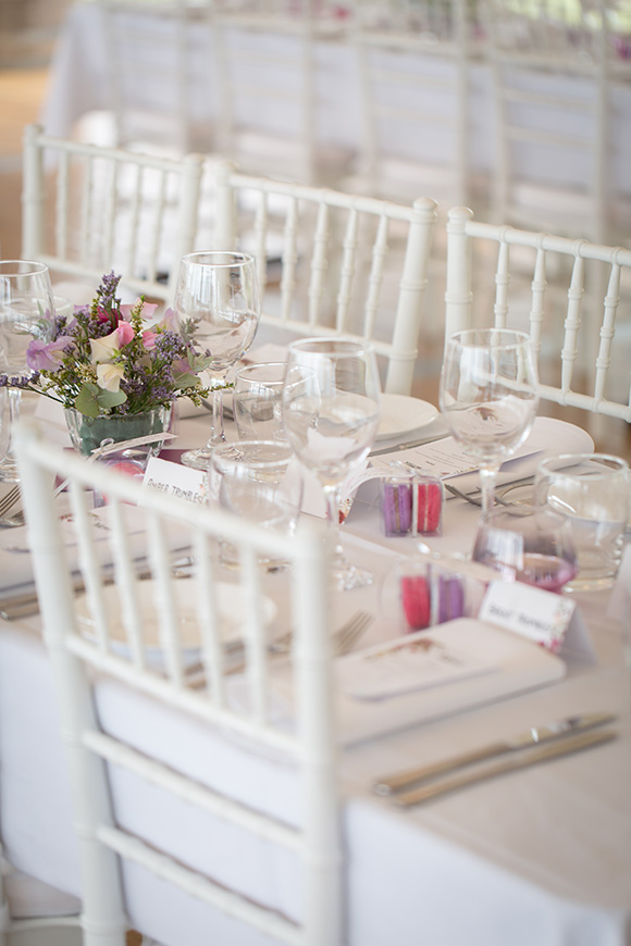 Wedding table at reception with white Tiffany chairs, white linen and pink and purple flowers.