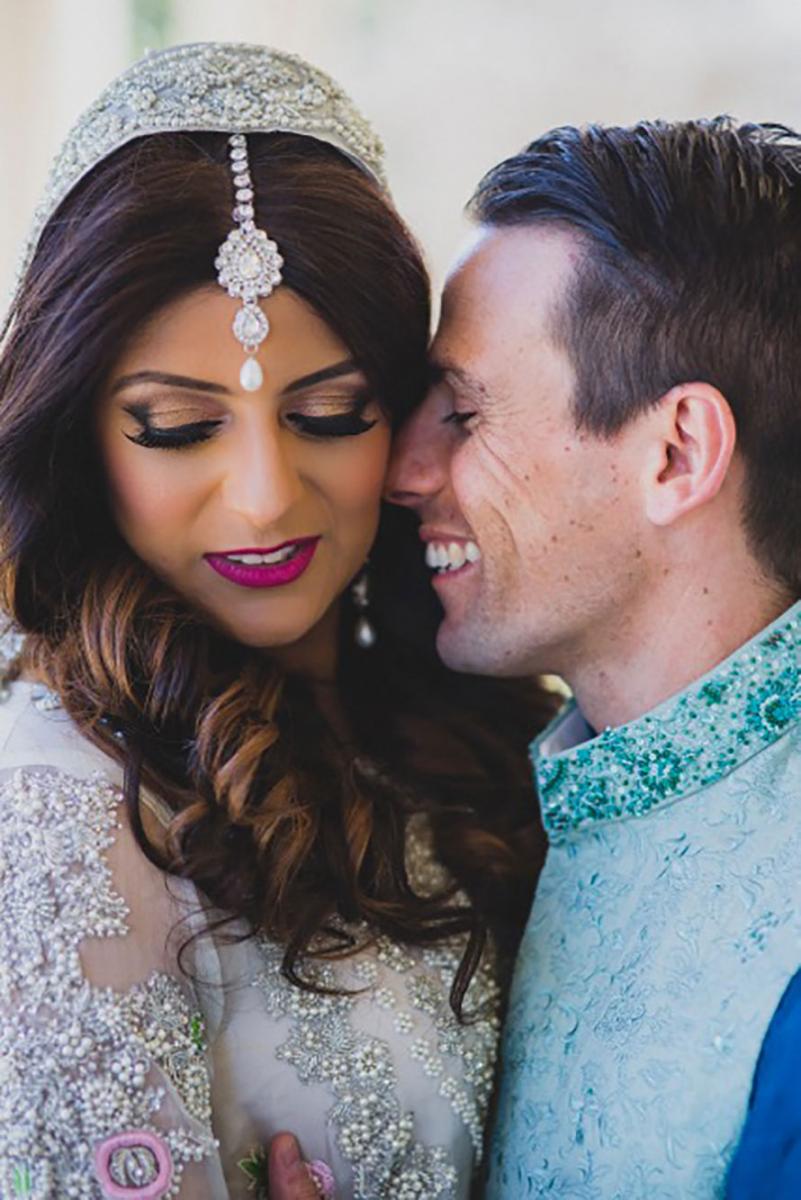 Multicultural wedding showing groom smiling and facing bride.