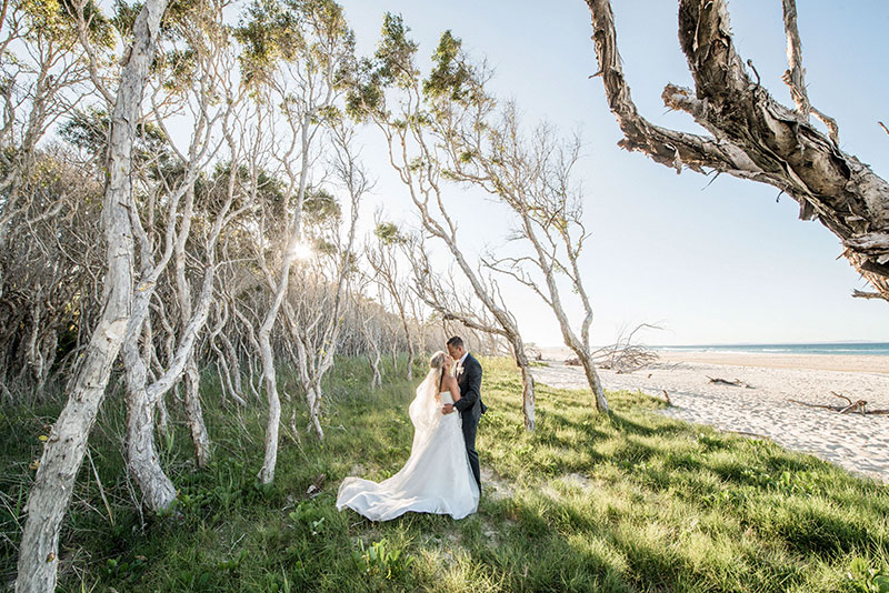 Bride and Groom hug amongst the trees on Stradbroke Island beach.