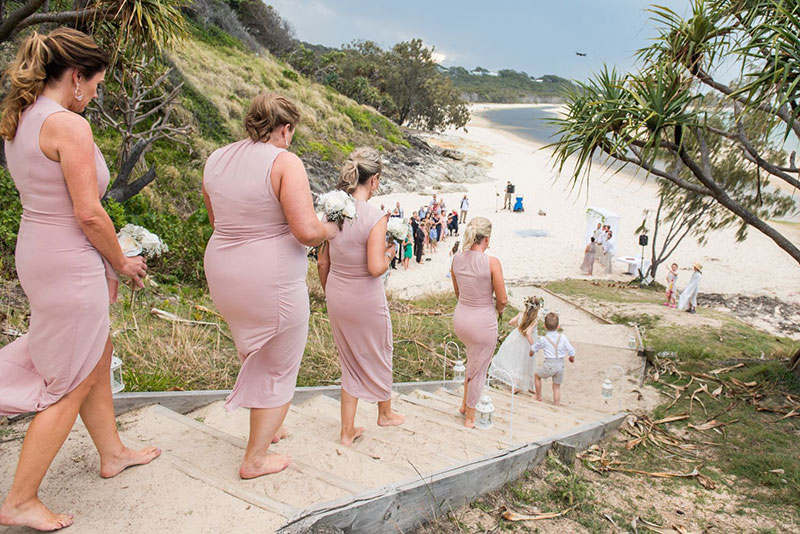 Bridesmaids walk down the stairs for a beach wedding.