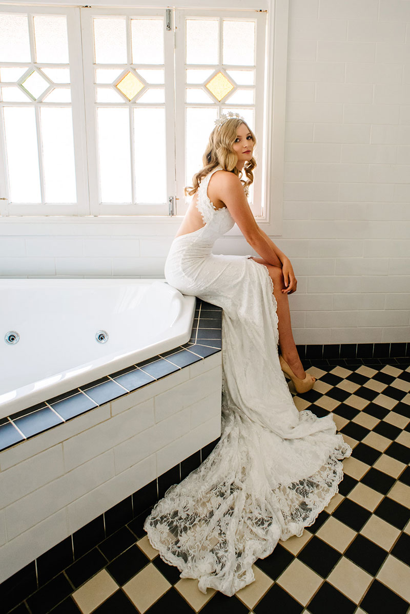 Bride sitting on edge of spa wearing a wedding gown with a front split.