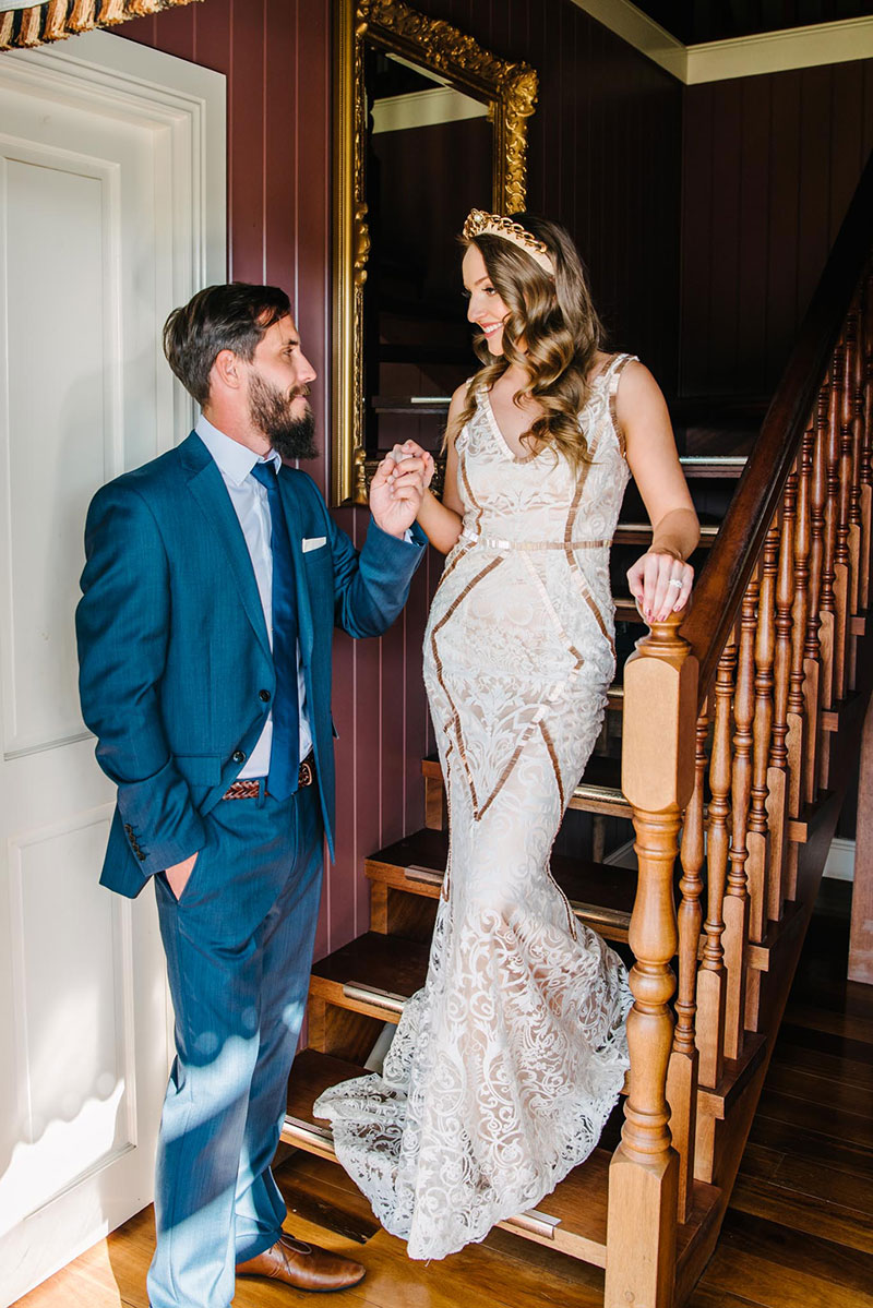 Bride in stunning geometric designed wedding dress and groom on stairs.