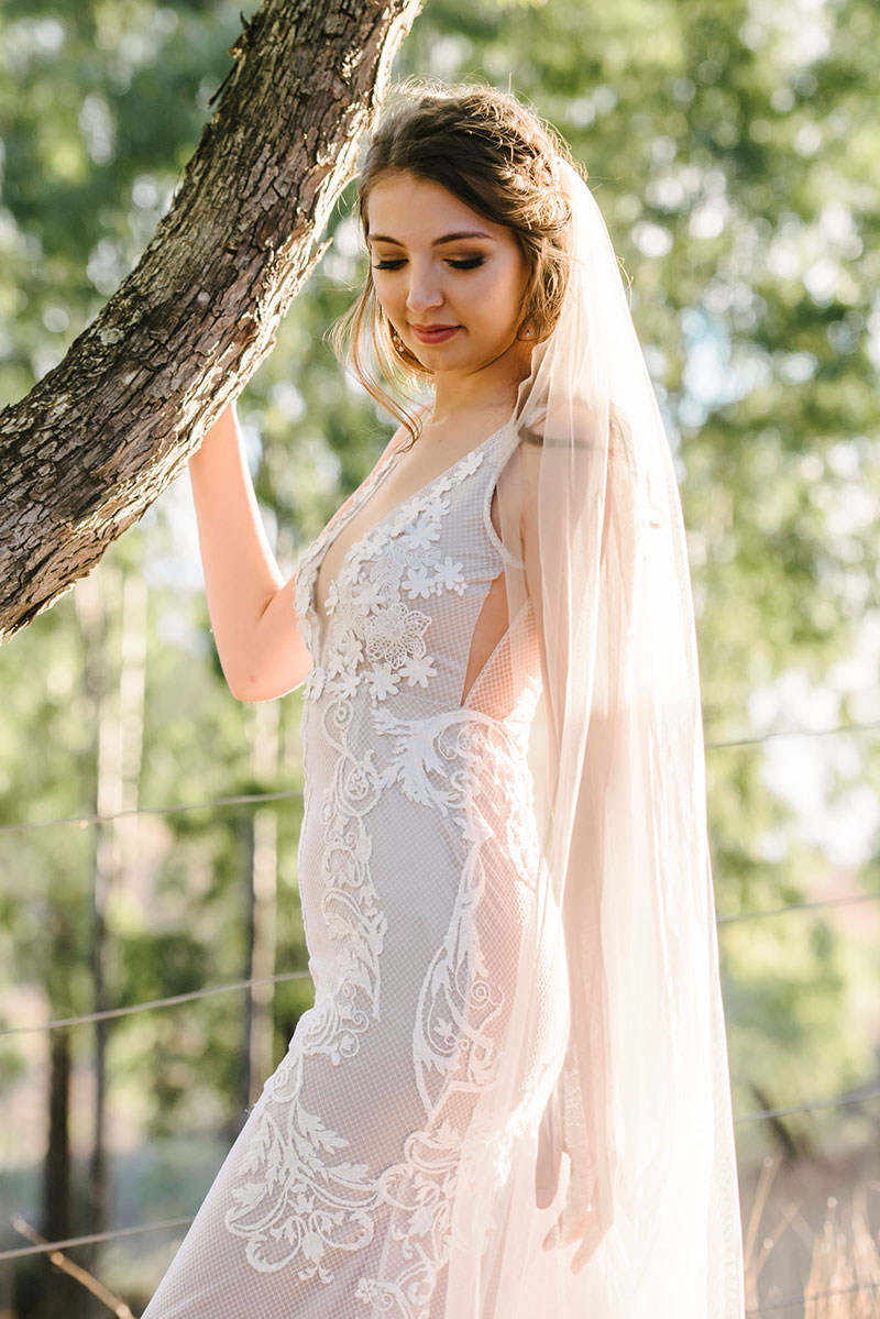 Bride in a gorgeous wedding gown standing outside near a tree.