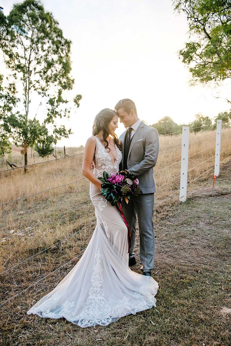 Bride in unique wedding gown, holding flowers, with groom.