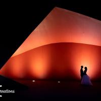 Bride and Groom stand in front of a lit up red coloured structure.