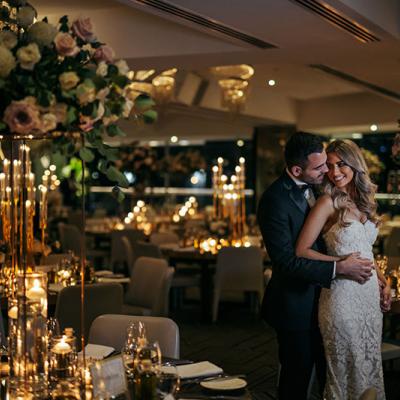 Happy Bride and Groom hold eachother in an opulent function room filled with flowers and tea lights.
