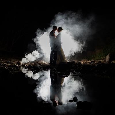 Photo of couple at night standing in front of a light and smoke bomb.