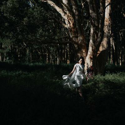 Moody photo showing a bride holding flowers walking near trees in the dark.