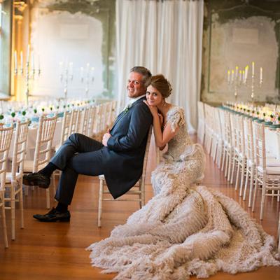 Bride in extravagent wedding gown poses with Groom inside an exquisite reception room.