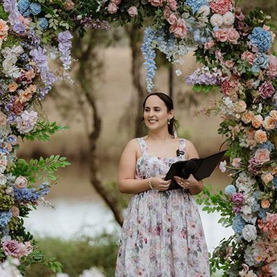 Photo of Kiara, Authorised Marriage Celebrant from Married by Kiara, standing amongst a beautiful flower arbor.